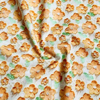 Longan Craft's Multicolor Printed Lawn Fabric by the Yard features soft pure cotton with large orange and yellow floral prints and green leaves on a white background. Visible folds and creases add subtle texture to this soft floral lawn material.