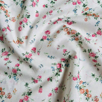 Longan Craft’s Multicolor Printed Lawn Fabric by the Yard features a soft white cotton lawn with a delicate floral pattern of small pink, orange, and blue flowers with green leaves, lightly wrinkled and gathered in the center.