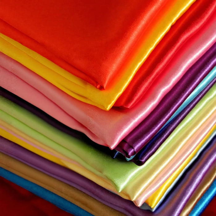 A close-up displays vibrant, neatly stacked Multicolor Satin Fabric By The Yard from Longan Craft—silky polyester satin in red, yellow, pink, purple, green, and blue—ideal for creative apparel or textile projects.