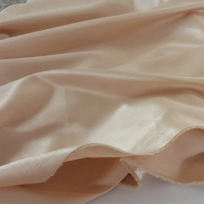 A close-up of the Multicolor Satin Fabric by Longan Craft shows its light beige, silky polyester satin with a subtle sheen, loosely draped and softly folded to reveal its delicate texture and unfinished edge—ideal for apparel.
