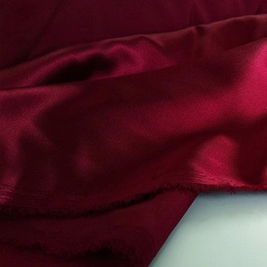 A close-up of Longan Craft’s Multicolor Satin Fabric By The Yard shows its silky polyester satin draped in soft folds, with a frayed edge against a light background. The smooth, shiny textile beautifully reflects the light—perfect for apparel.