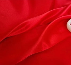 A close-up of Longan Craft Multicolor Satin Fabric by the yard shows its silky polyester satin texture with vibrant red folds and a hint of a white object in the top right corner—perfect textile for apparel.