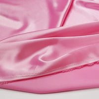 A close-up of Longan Craft's Multicolor Satin Fabric by the Yard shows smooth, shiny pink silky polyester satin with gentle folds and a glossy sheen, perfect for apparel and textile projects.