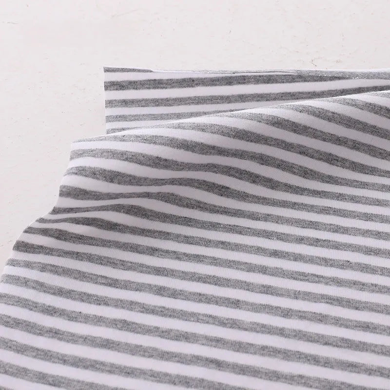 A close-up shows Longan Craft's Multicolor Striped Cotton Jersey Fabric by the yard, a stretch elastane sports jersey material with horizontal gray and white stripes, slightly wrinkled and layered on a light surface.