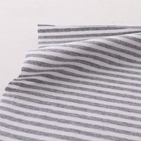A close-up shows Longan Craft's Multicolor Striped Cotton Jersey Fabric by the yard, a stretch elastane sports jersey material with horizontal gray and white stripes, slightly wrinkled and layered on a light surface.