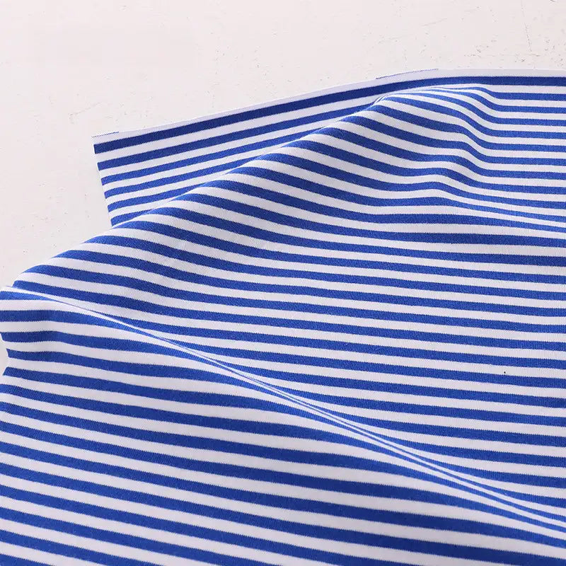 The Longan Craft Multicolor Striped Cotton Jersey Fabric by the yard, a stretch elastane sports jersey material, is displayed on a white surface with gentle folds and visible blue and white stripes.