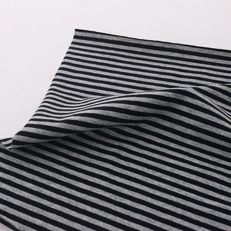 A piece of Longan Craft Multicolor Striped Cotton Jersey Fabric By The Yard is displayed on a white surface, with black and gray stripes visible and part gently folded to showcase its soft, stretchy sports jersey material.