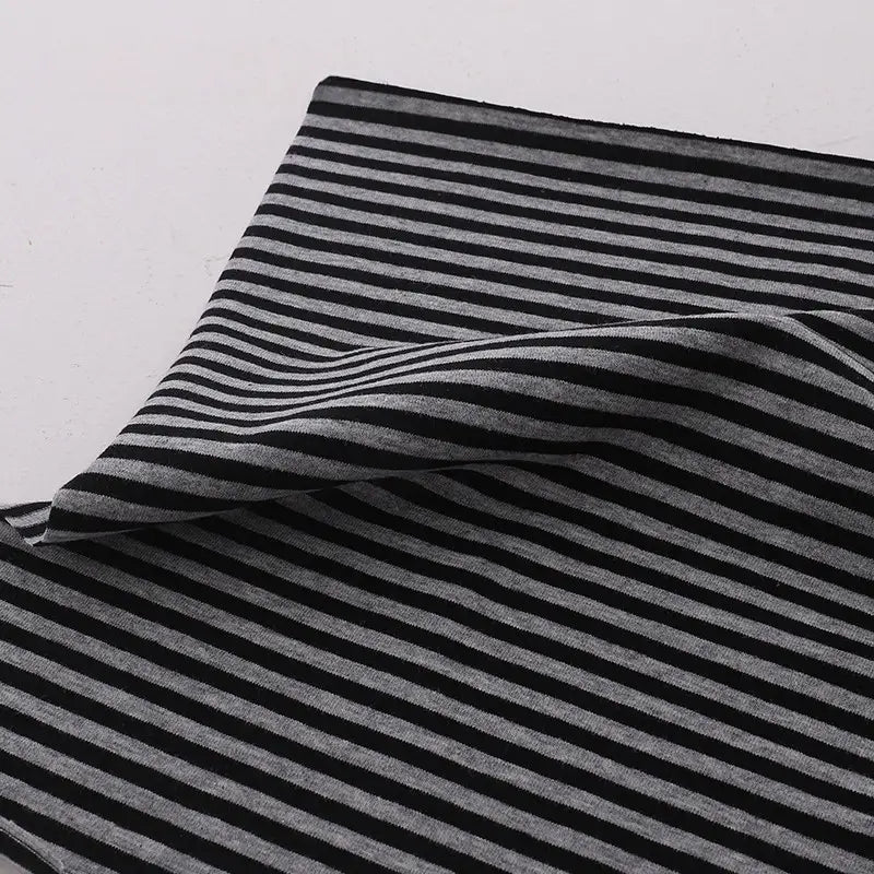 A close-up of Multicolor Striped Cotton Jersey Fabric By The Yard from Longan Craft, featuring stretch elastane jersey material in black and gray stripes with a folded corner, showcasing the sports jersey fabric's texture on a white background.