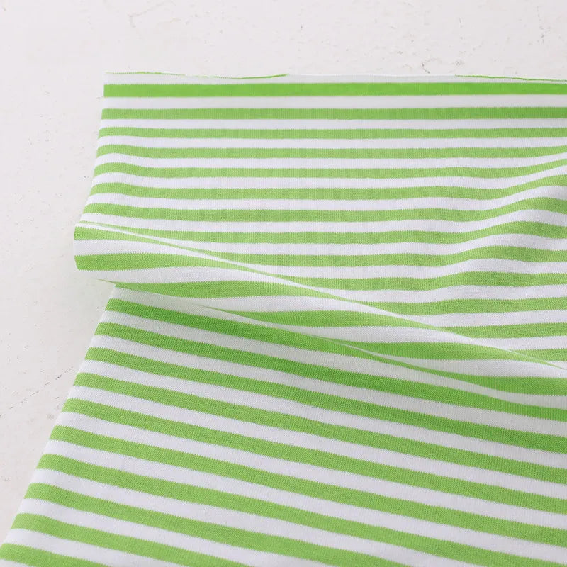 A piece of Longan Craft’s Multicolor Striped Cotton Jersey Fabric By The Yard, a soft stretch elastane sports jersey material, is laid out on a light surface with gentle folds near the top left corner.