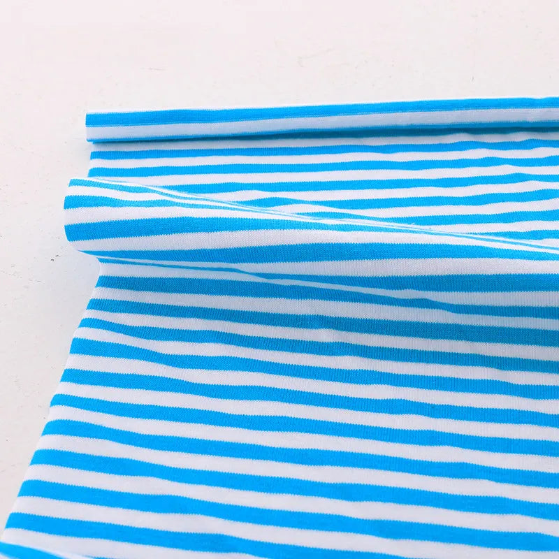 The Multicolor Striped Cotton Jersey Fabric by Longan Craft is shown laid flat, one edge rolled to display its stretch and vibrant pattern—ideal sports jersey material by the yard.