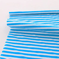 The Multicolor Striped Cotton Jersey Fabric by Longan Craft is shown laid flat, one edge rolled to display its stretch and vibrant pattern—ideal sports jersey material by the yard.