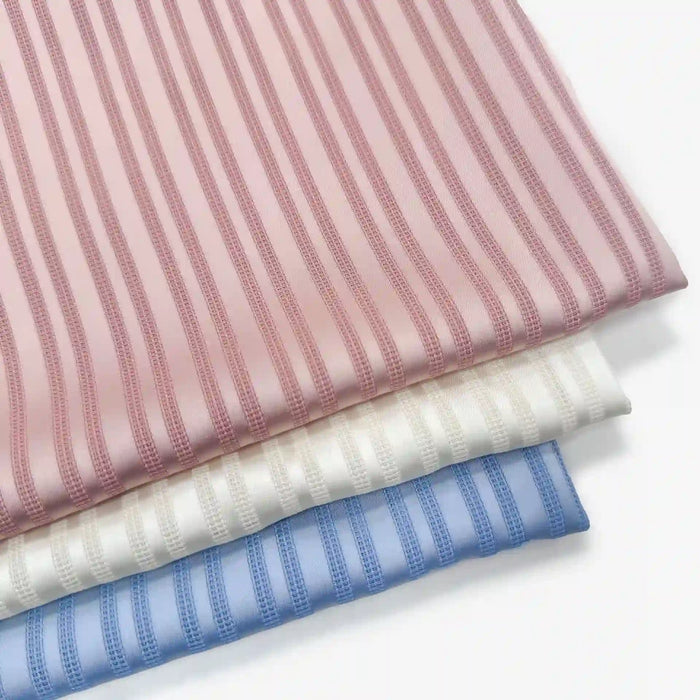 Three neatly stacked pieces of Longan Craft Multicolor Striped Polyester Dobby Fabric: pink on top, white in the middle, blue at the bottom. Each features alternating wide and narrow stripes—soft, smooth, and ideal for apparel by the yard.