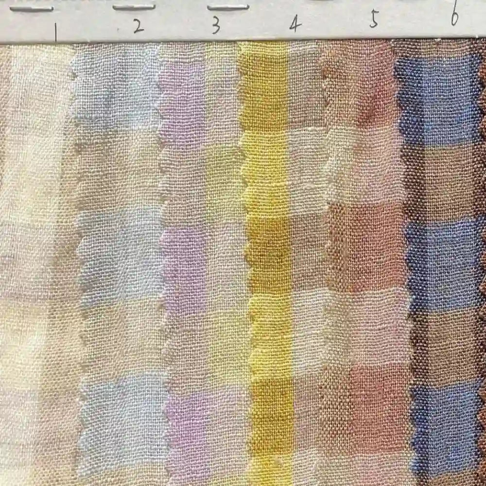 A swatch of Longan Craft’s Multicolor Washed Plaid Linen Fabric By The Yard is shown, featuring vertical stripes in pastel shades and scalloped edges between some of the stripes. The ruler at the top is marked from 2 to 6 cm, highlighting the scale of this vintage checkered pure linen material, perfect for casual wear.