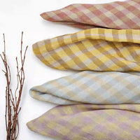 Four folded pieces of the Longan Craft Multicolor Washed Plaid Linen Fabric By The Yard—with vintage checkered designs in pink, yellow, blue, and purple—are arranged horizontally. To the left on the white background, several thin bare twigs are displayed.