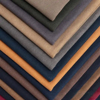A diagonal stack of Longan Craft’s Multicolor Waxed Cotton Canvas by the yard shows solid brown, beige, gray, blue, orange, and burgundy waterproof cotton fabric—moisture-proof and ideal for outdoor clothing.