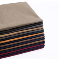 A stack of folded Longan Craft Multicolor Waxed Cotton Canvas Fabric features brown, navy blue, mustard yellow, maroon, and burgundy waterproof cotton fabric by the yard, perfect for outdoor clothing, set against a white background.