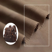 Close-up of Longan Craft Multicolor Waxed Cotton Canvas Fabric with zigzag-cut edges, shown next to a small brown backpack. This 100% waterproof, moisture-proof fabric is perfect for outdoor clothing and is sold by the yard.