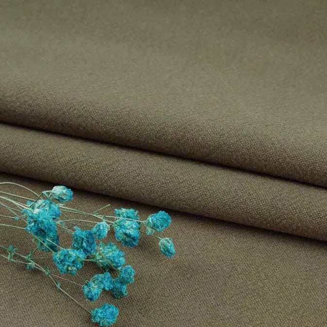 A close-up of Longan Craft’s Multiple Colors Linen Fabric By The Yard, a durable washed cotton linen blend clothing material in olive green, shown folded with bright blue dried flowers placed on top.