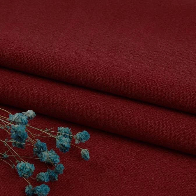 Folded Longan Craft Multiple Colors Linen Fabric By The Yard, a washed cotton linen blend with a matte finish, is displayed with small blue dried flowers in the lower left corner.