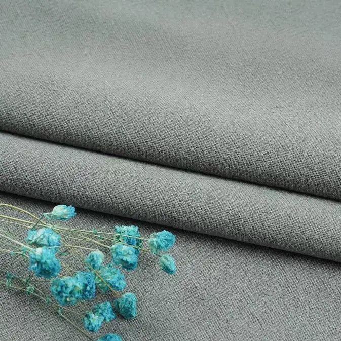 A folded light gray Longan Craft linen fabric by the yard, made from a washed cotton-linen blend for breathable and durable apparel, with small blue dried flowers placed on top.