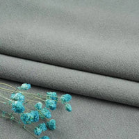 A folded light gray Longan Craft linen fabric by the yard, made from a washed cotton-linen blend for breathable and durable apparel, with small blue dried flowers placed on top.