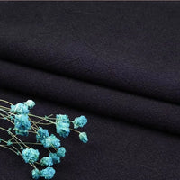 A close-up of Longan Craft’s Multiple Colors Linen Fabric by the Yard, a washed cotton linen blend for apparel, in solid black, with delicate blue dried flowers accentuating the breathable, durable natural fibers.