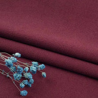 A sprig of small, dried blue flowers lays on neatly folded maroon linen fabric by Longan Craft—washed cotton linen blend by the yard, offering softness, breathability, and durability for apparel and clothing projects.