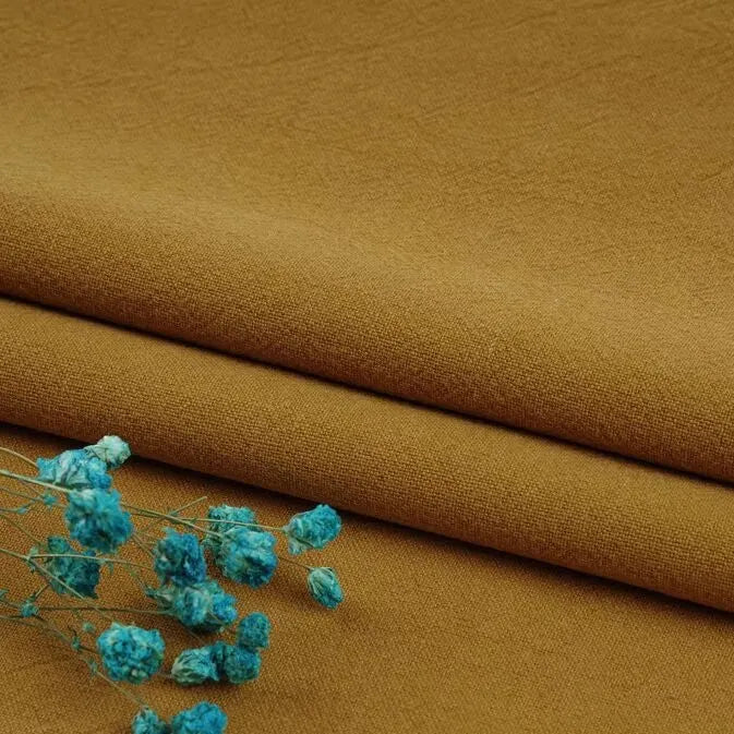 A close-up of Longan Craft’s Multiple Colors Linen Fabric By The Yard—a washed cotton linen blend—shows its durable, breathable fibers, folded neatly with a small bunch of blue dried flowers on top.