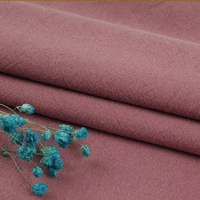 Three pieces of mauve "Multiple Colors Linen Fabric By The Yard" from Longan Craft are stacked, with blue dried flowers placed on the linen cotton blend fabric in the lower left corner.