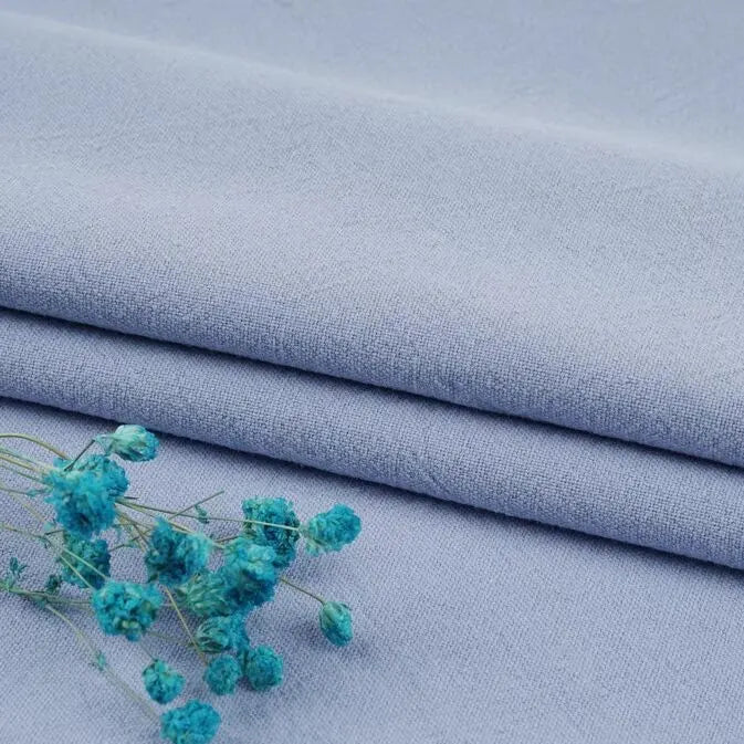 Longan Craft’s Multiple Colors Linen Fabric by the Yard is a washed cotton linen blend for apparel, shown here in light blue. Soft, breathable, and slightly textured, it's neatly folded with turquoise dried flowers on top.