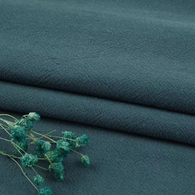 Three neatly folded pieces of Longan Craft’s Multiple Colors Linen Fabric by the Yard, a washed cotton linen blend for apparel, in dark teal. The soft, textured fabric is breathable and durable, with dried teal flowers resting on top.