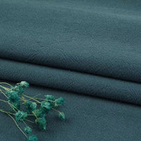 Three neatly folded pieces of Longan Craft’s Multiple Colors Linen Fabric by the Yard, a washed cotton linen blend for apparel, in dark teal. The soft, textured fabric is breathable and durable, with dried teal flowers resting on top.