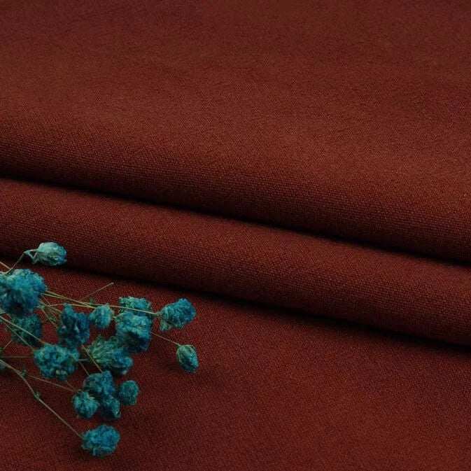 A close-up of Longan Craft’s Multiple Colors Linen Fabric By The Yard, a durable washed cotton linen blend for apparel, in dark reddish-brown with blue dried flowers on top. The natural fiber texture and contrasting colors are visible.