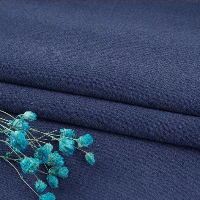 A close-up of folded dark blue Multiple Colors Linen Fabric By The Yard from Longan Craft, a durable washed cotton linen blend for apparel, with small blue dried flowers on top highlighting the texture and color contrast.