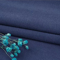 A close-up of folded dark blue Multiple Colors Linen Fabric By The Yard from Longan Craft, a durable washed cotton linen blend for apparel, with small blue dried flowers on top highlighting the texture and color contrast.