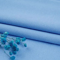 Two pieces of light blue Longan Craft Multiple Colors Linen Fabric are neatly folded, with a sprig of dried blue flowers placed on the Washed Cotton Linen Blend material in the lower left corner.