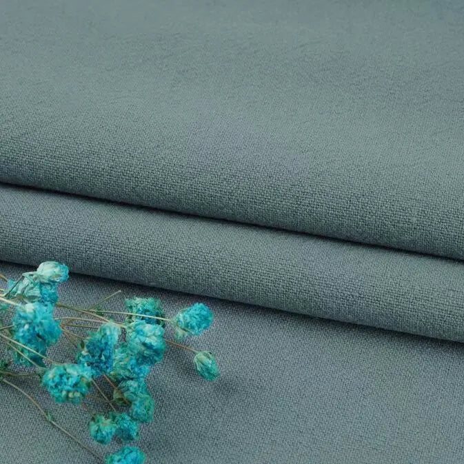 A close-up of Longan Craft’s Washed Cotton Linen Blend Fabric in gray from their Multiple Colors collection, folded with a small bunch of blue dried flowers resting on top.