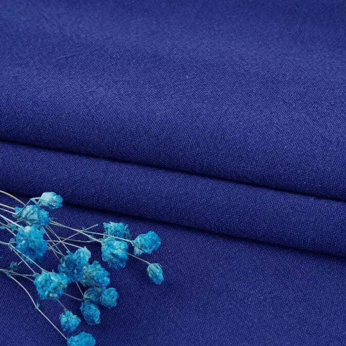 A close-up of two folded pieces of Longan Craft Multiple Colors Linen Fabric By The Yard in deep blue, accented with small dried blue flowers for an elegant, soft look. Durable washed cotton linen blend, perfect for apparel.