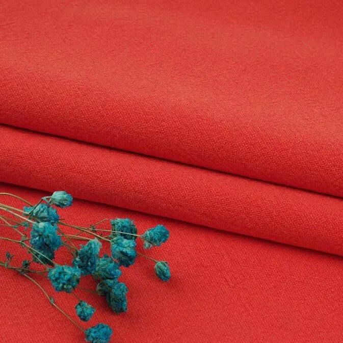Two pieces of bright red Multiple Colors Linen Fabric By The Yard from Longan Craft are stacked neatly, with small blue dried flowers on top, creating a vivid contrast on the durable washed cotton linen blend material for apparel.