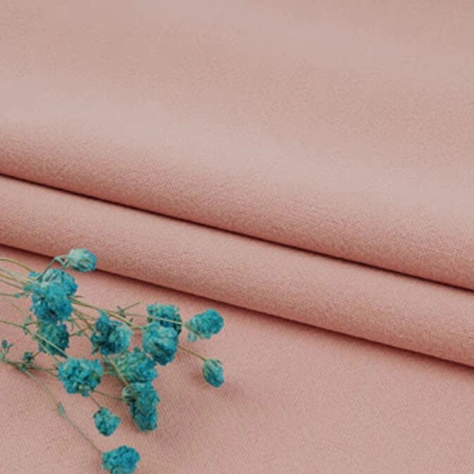 A sprig of small blue dried flowers rests on neatly folded, soft pink Multiple Colors Linen Fabric By The Yard—washed cotton linen blend clothing material by Longan Craft.