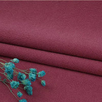 Folded maroon Multiple Colors Linen Fabric by the yard from Longan Craft, a durable washed cotton linen blend for apparel, with a textured surface. A small bunch of blue dried flowers lies on the lower left side.