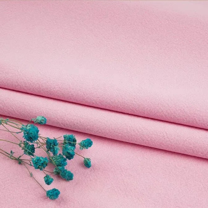 A trio of neatly folded, light pink linen fabric from Longan Craft rests beneath a small sprig of turquoise dried flowers. This washed cotton-linen blend is perfect for apparel and available in multiple colors by the yard.