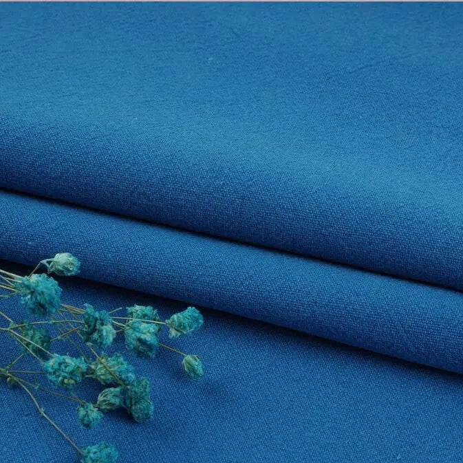 A close-up of Longan Craft's Multiple Colors Linen Fabric By The Yard shows its soft, smooth washed cotton linen blend, with a dried blue flower on top—perfect breathable, durable material for apparel.