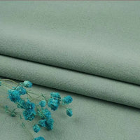 A close-up of Longan Craft’s sage green washed cotton linen blend fabric by the yard, featuring its textured surface with a small cluster of blue dried flowers placed on top.
