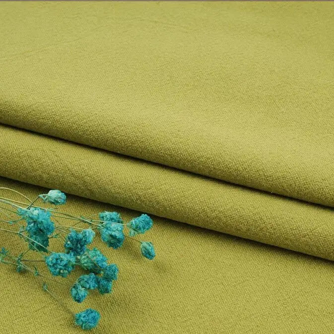 A few sprigs of small blue flowers rest on neatly folded, olive-green fabric from Longan Craft's Multiple Colors Linen Fabric by the Yard—washed cotton linen blend, perfect for durable apparel.