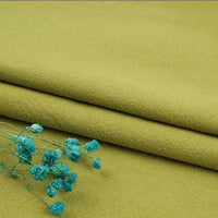 A few sprigs of small blue flowers rest on neatly folded, olive-green fabric from Longan Craft's Multiple Colors Linen Fabric by the Yard—washed cotton linen blend, perfect for durable apparel.