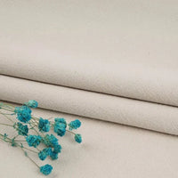 Two folded pieces of Longan Craft’s Multiple Colors Linen Fabric By The Yard, a washed cotton linen blend for apparel, are displayed on a flat surface. A small sprig of dried blue flowers adds color to the neutral background.