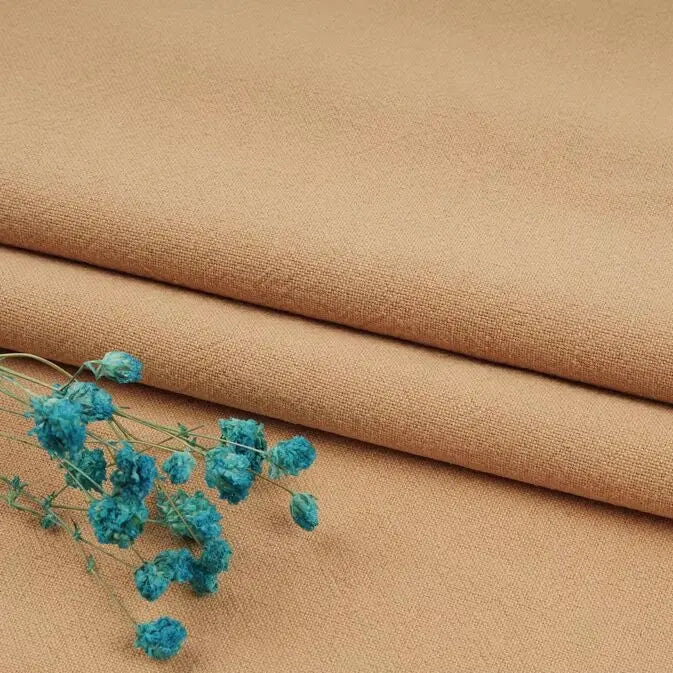 A close-up of folded tan Multiple Colors Linen Fabric By The Yard from Longan Craft, a washed cotton linen blend for apparel, with a small bunch of dried blue flowers placed on top.