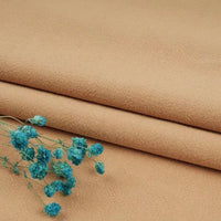 A close-up of folded tan Multiple Colors Linen Fabric By The Yard from Longan Craft, a washed cotton linen blend for apparel, with a small bunch of dried blue flowers placed on top.
