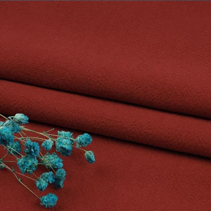 A close-up of two neatly folded pieces of Longan Craft's washed cotton linen blend fabric in dark red, with breathable natural fibers, topped with vibrant blue dried flowers. Multiple Colors Linen Fabric By The Yard, ideal for apparel.